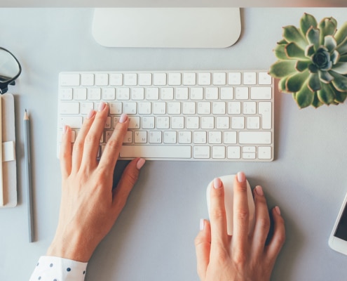 Hands typing on a white keyboard at a minimalist desk setup with a notebook, glasses, and a succulent plant. SEO for therapists starts with small, focused actions like optimizing content and tracking keywords.