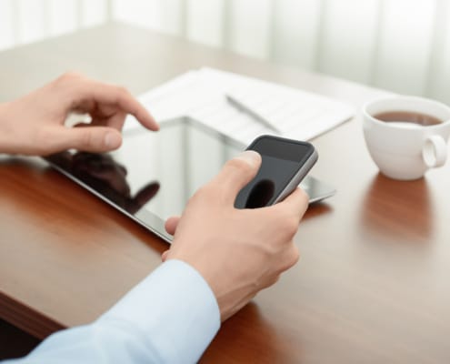 business person typing on a phone and ipad tablet while sitting at a desk. Le