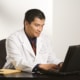 An Asian american male doctor typing on a black laptop at his desk. Our SEO for functional medicine doctors is here to help you wellness website rank higher on Google. Find your ideal clients today with our SEO services.