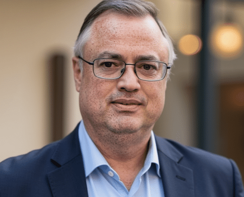 Edward Walker – Co-owner of Simplified SEO Consulting, with short gray hair and glasses wearing a dark suit jacket over a light blue shirt, standing outside with blurred warm lighting behind him.