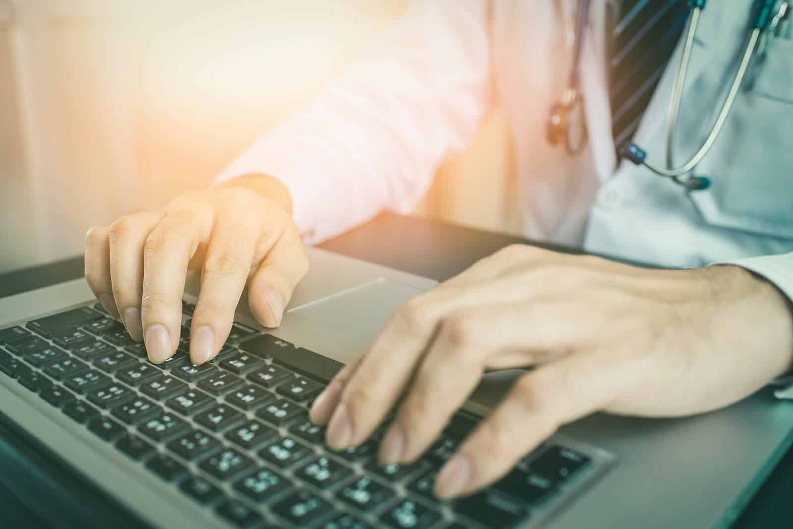 doctor on laptop | seo for holistic health and wellbeing | seo for functional medicine | doctor seo consulting | Montana | North Carolina | Virginia Doctor typing on a laptop in clinic office. Find more of your ideal clients with seo for holistic health and wellbeing and professional doctor seo consulting.