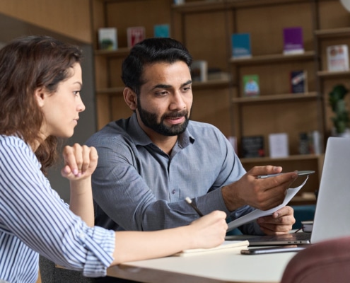 Man helping woman while sitting at a table pointing to a laptop. Discover how to find your ideal client and improve your private practice SEO today.