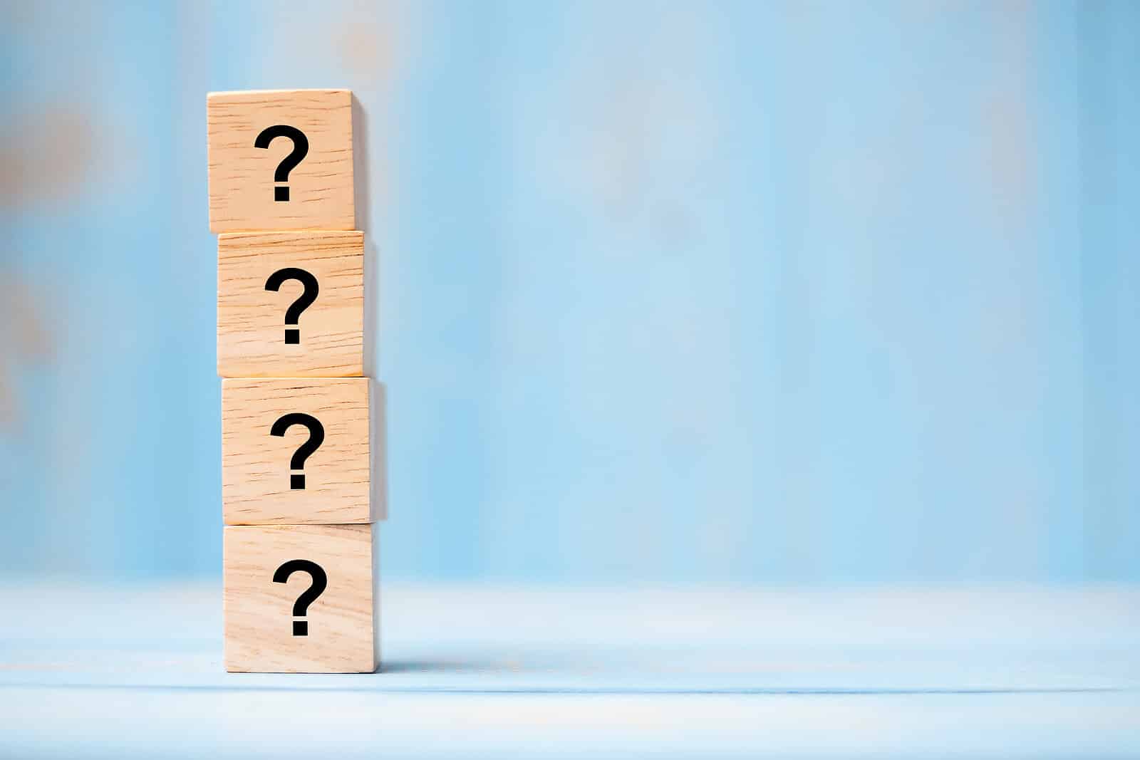 Stacked wooden blocks with question marks against a blue background, illustrating common questions SEO for holistic health and wellbeing can answer.