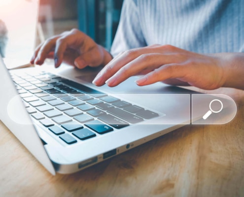 Hands typing on a laptop keyboard with a digital search bar overlay, representing SEO for holistic health and wellbeing.