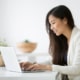 Happy woman sitting at a desk smiling while typing on a laptop. Learn to improve your private practice SEO and begin to find your ideal clients with the support of Simplified SEO Consulting.