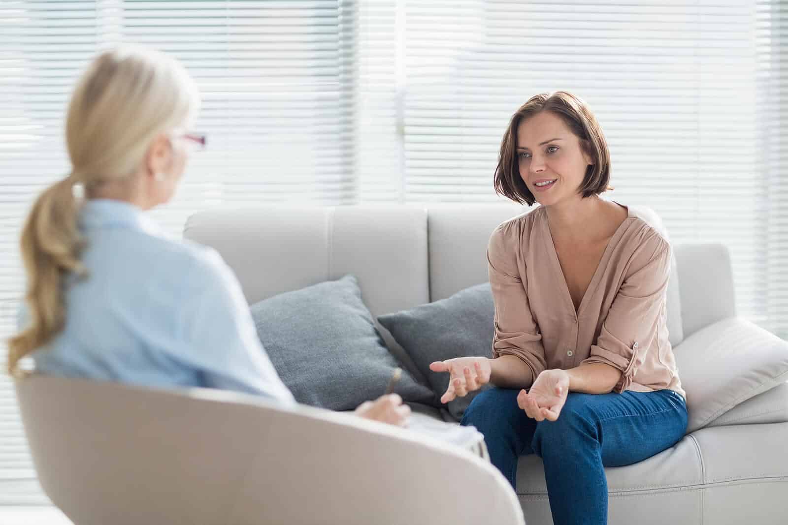 Woman sitting on a couch speaking to an older woman in a chair. This image represents how you can find your ideal client for your therapy practice and begin to help those in need. Improve your private practice SEO with Simplified SEO Consulting soon.