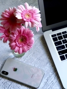 An Iphone sitting near pink flowers in a vase & a laptop. Social media management can help you attract your ideal clients through Instagram, Facebook & more. Reach out today to get started!