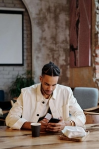 Young man in a café browsing his phone, representing how patients increasingly search for health information online—highlighting the need for SEO for functional medicine and the value of working with a medical practices SEO consultant.