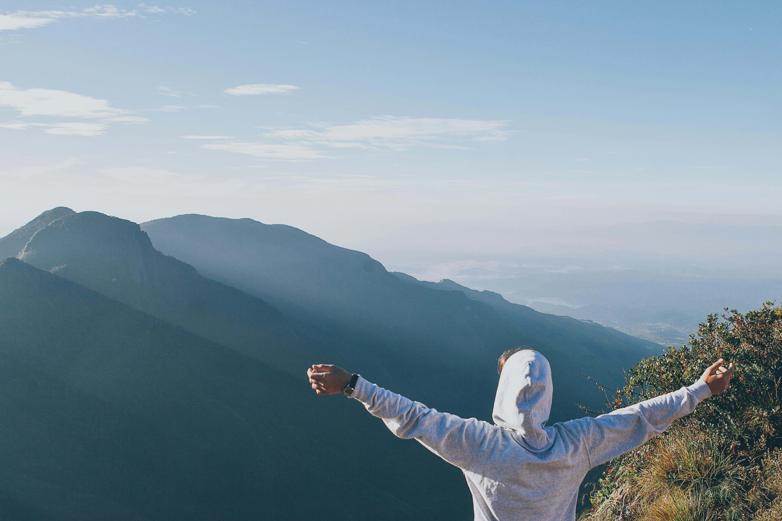Person standing on a mountain with arms open wide, symbolizing the expansive growth and visibility that holistic SEO can bring to wellness practitioners online.
