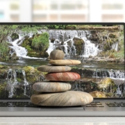 A stack of multicolored zen stones sits atop a laptop displaying a waterfall scene, blending technology with integrative medicine SEO. Are you considering how SEO consulting services could strengthen your clinic’s digital presence? Thoughtful strategy aligns care with visibility.