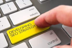 Finger pressing a bright yellow keyboard key labeled “Developing SEO Strategy,” illustrating how technical SEO services and private practice SEO work together to build SEO for online therapy services that attract ideal clients. 