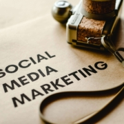 "Social media marketing" on a piece of paper near a camera. Discover how social media marketing can increase your connection with clients. Contact us today for a social media manager.