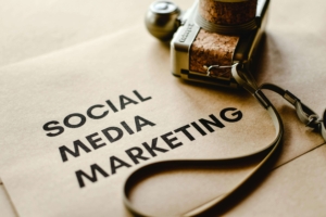 "Social media marketing" on a piece of paper near a camera. Discover how social media marketing can increase your connection with clients. Contact us today for a social media manager. 