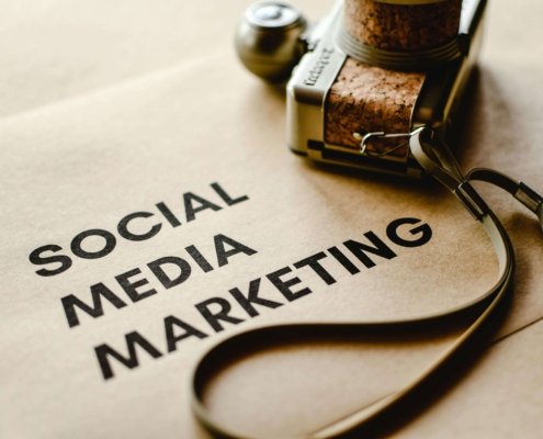 "Social media marketing" on a piece of paper near a camera. Discover how social media marketing can increase your connection with clients. Contact us today for a social media manager.