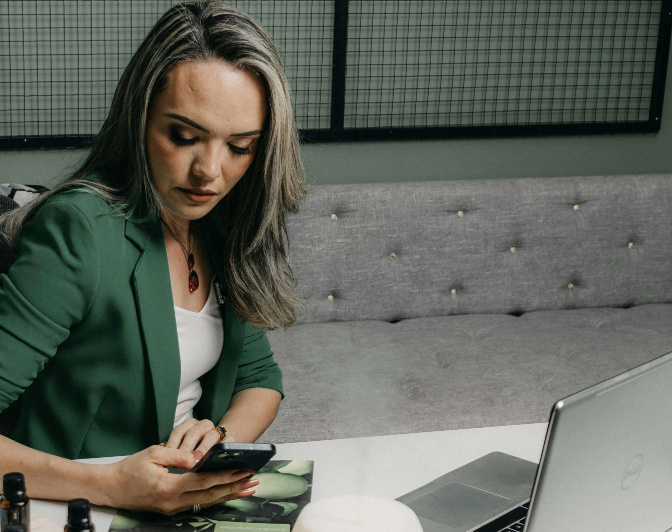 A holistic practitioner sitting at her desk with essential oils and a laptop, checking her phone while preparing for work. With the support of holistic SEO, you're ideal client can begin to find your website through search results.
