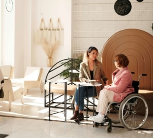 A therapist sitting talking to a client who is handicapped in a coffee shop. A social media manager helps you reach ideal clients by posting consistently. Reach out to learn more!