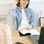 Smiling woman with glasses reviewing notebooks at her desk with a laptop, representing how SEO consultants and SEO consulting services help therapists create authentic, human-centered content for their practice websites.