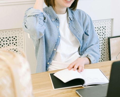 Smiling woman with glasses reviewing notebooks at her desk with a laptop, representing how SEO consultants and SEO consulting services help therapists create authentic, human-centered content for their practice websites.