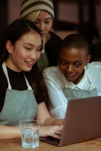 Three women smiling and collaborating around a laptop, representing how search engine optimization for therapists and a strong therapist SEO strategy help practitioners create content that connects with ideal clients.