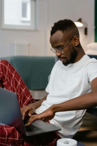 Man with glasses working on a laptop from his couch, representing how SEO consulting services and SEO consultants help therapists create and edit AI content from anywhere without losing their authentic voice.