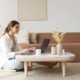 Woman sitting on the floor working on a laptop at a coffee table in a cozy living room, representing how SEO consultants and SEO consulting services help therapists create authentic content for their practice from anywhere.