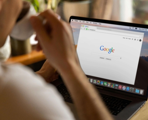 Person typing on Google on a laptop while sipping from a mug, representing research related to SEO consulting services at Simplified SEO Consulting.