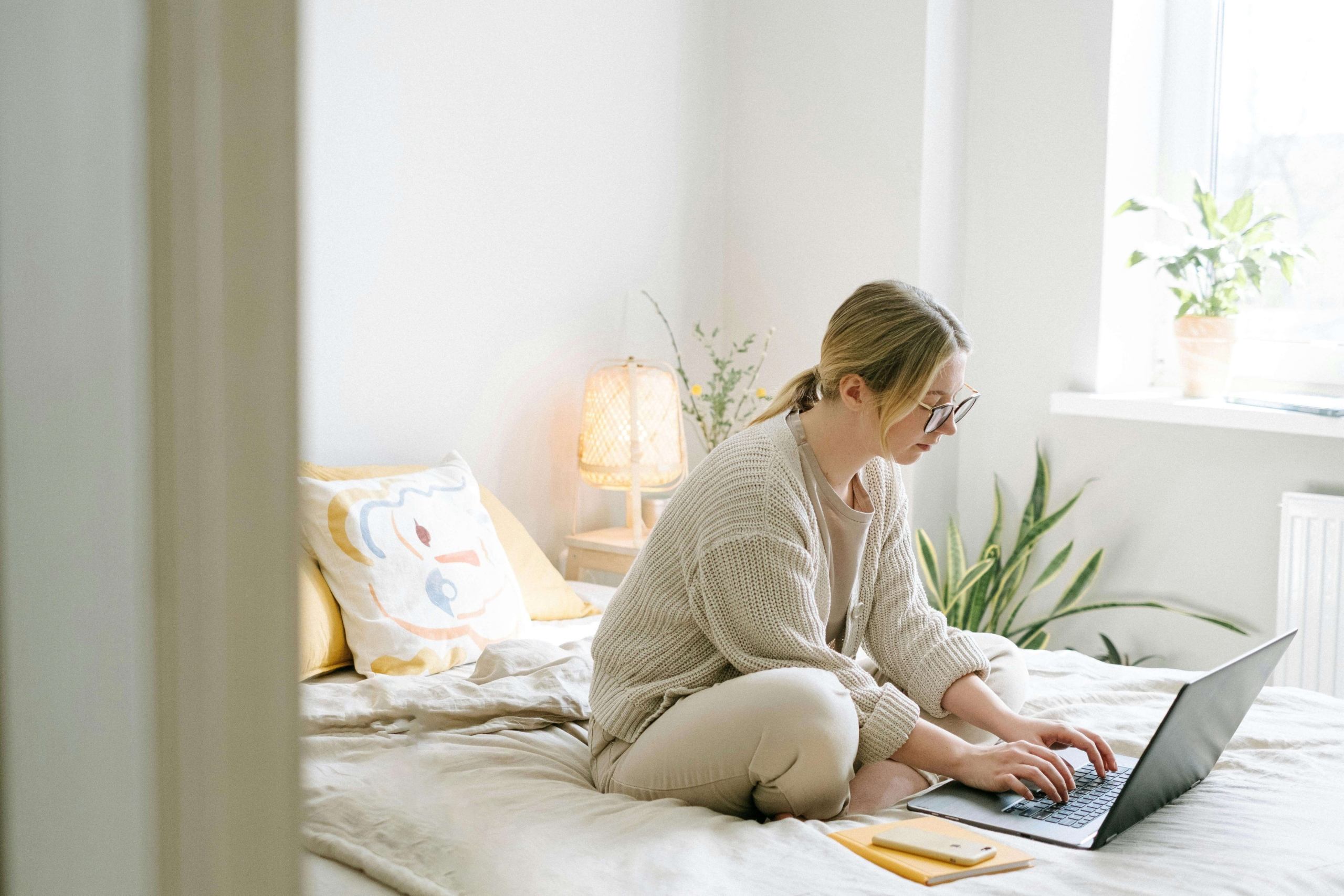 Woman sitting on bed using a laptop, looking thoughtful, reflecting strategy and planning offered through SEO consulting services at Simplified SEO Consulting.