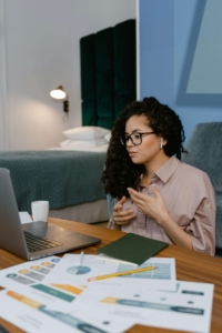 Woman with glasses reviewing printed analytics reports at a desk while on a video call, representing how SEO consulting services and SEO help for therapists use data from tools like Google Search Console to guide content strategy.
