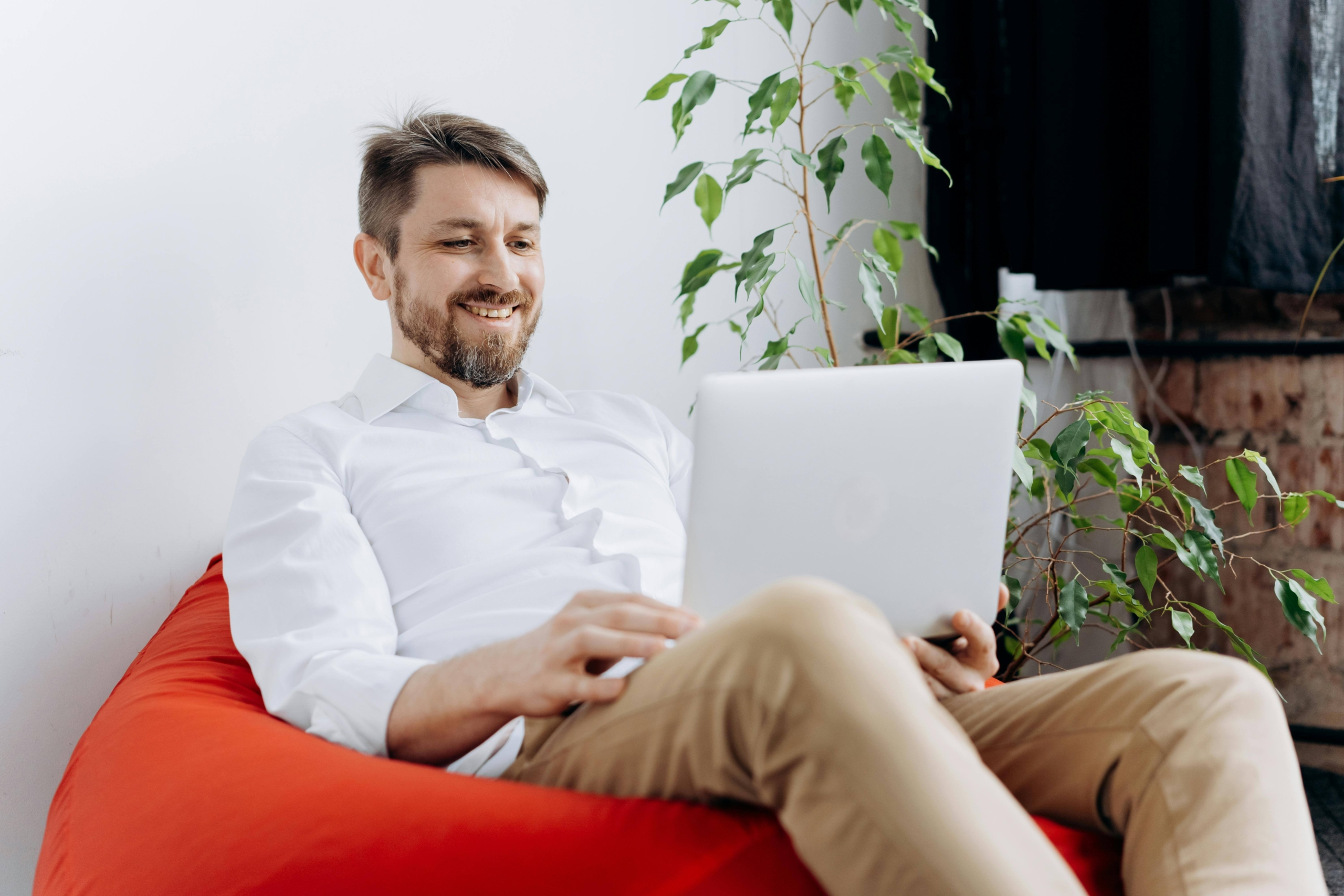Man smiling while using a laptop on a beanbag chair, illustrating productive results from SEO consulting services at Simplified SEO Consulting.