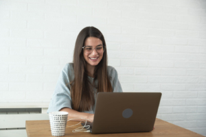 Woman smiling while working on a laptop, representing a therapist creating content that feels human and supportive. This relates to keywords for therapists, seo keywords for therapists, and keywords for online counseling pages that help the right clients find care on Google.