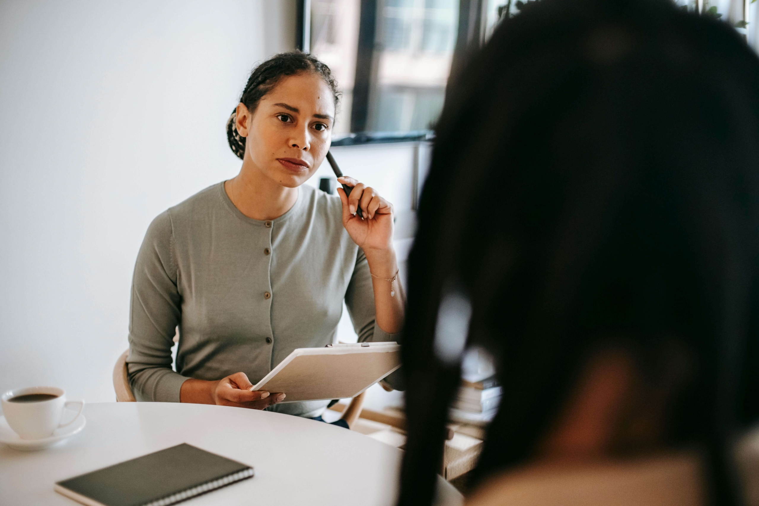 A therapist sitting across from a client, holding a clipboard and pen, listening attentively during a session. Your clients deserve to find you. Get the SEO help for therapists you need with Simplified SEO Consulting.