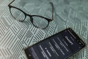 Glasses and a smartphone displaying the ChatGPT interface on a patterned surface, illustrating how therapists use AI tools alongside keywords for therapists and seo for therapy practice strategies to create effective website content.