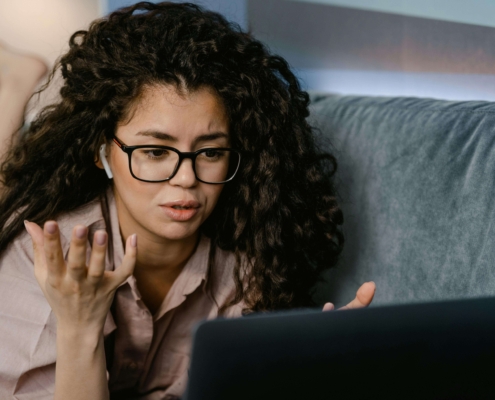 Woman lying on a couch using a laptop, talking to someone in a virtual therapy session, illustrating online engagement supported by SEO for online therapy services.