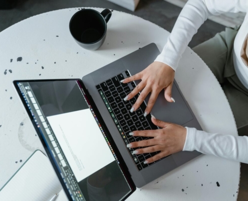 Overhead view of a woman typing on a laptop at a round table with a coffee mug, representing how SEO for therapists and SEO consulting services help practitioners create and refine AI-assisted content for their practice websites.