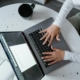 Overhead view of a woman typing on a laptop at a round table with a coffee mug, representing how SEO for therapists and SEO consulting services help practitioners create and refine AI-assisted content for their practice websites.