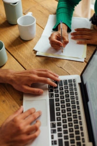 Two people collaborating at a wooden table with a laptop and handwritten notes, representing how SEO for mental health professionals and SEO for therapists involves hands-on strategy and intentional content planning.