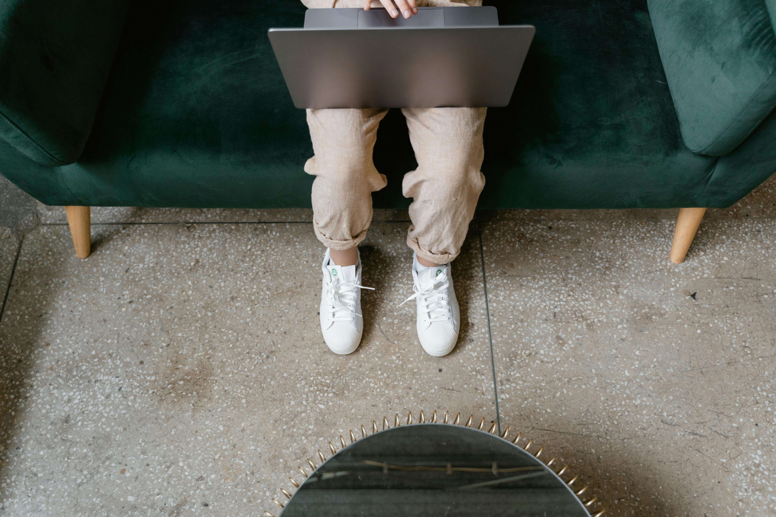 Person sitting on a green couch with a laptop on their lap, illustrating digital work and practice growth supported by SEO for online therapy services.