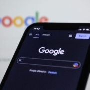 Close-up of a phone showing the Google homepage with the search bar visible, with a computer screen displaying the same page in the background, representing SEO for online therapy services.