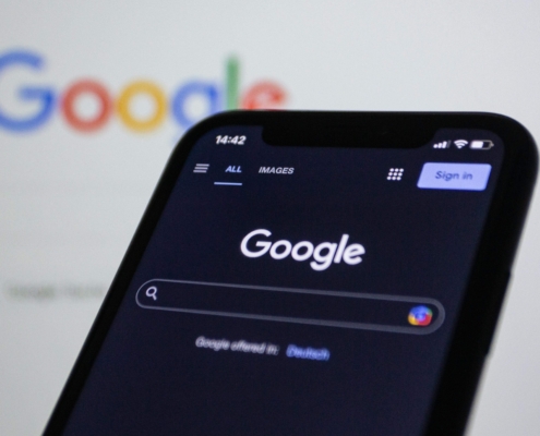 Close-up of a phone showing the Google homepage with the search bar visible, with a computer screen displaying the same page in the background, representing SEO for online therapy services.