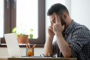 A man sits at his desk with his head in his hands, frustrated while looking at his laptop screen. Technical website issues like broken links, slow page speed, and indexing errors are common pain points in therapist SEO that can quietly hurt rankings without any obvious warning signs. 