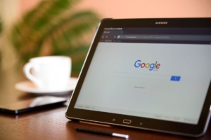 Tablet displaying the Google search homepage on a desk next to a coffee cup, representing how SEO consultants help with SEO for therapists by tracking search data and rankings during the summer slowdown.