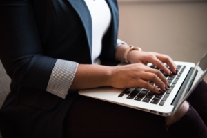 Close-up of a woman in a blazer typing on a laptop in her lap, representing how SEO services for therapists and local SEO for therapists help practices stay visible and keep growing through the summer slowdown.