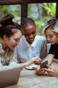 friends outside pointing to phone | social media manager | social media marketing for therapists | social media for therapists | st louis, mo | Ladue, MO | clayton, mo Three diverse women sitting together in a circle pointing at a phone. Representing social media marketing & sharing posts with friends. Discover how social media marketing can help you reach ideal therapy clients.