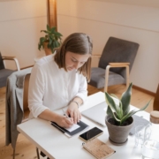 Woman writing in a notebook at a tidy desk with a laptop and plant nearby, representing how SEO consultants help with SEO for therapists by planning and refreshing content during the summer slowdown."