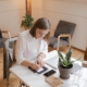 Woman writing in a notebook at a tidy desk with a laptop and plant nearby, representing how SEO consultants help with SEO for therapists by planning and refreshing content during the summer slowdown."