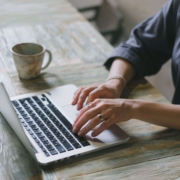 Close-up of a person working on a laptop with a coffee mug nearby, representing content creation and consistency in SEO help for therapists.