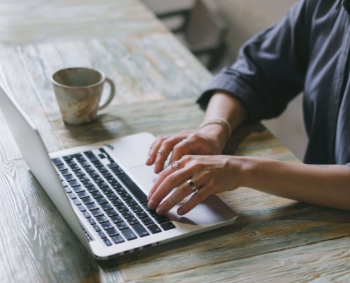 Close-up of a person working on a laptop with a coffee mug nearby, representing content creation and consistency in SEO help for therapists.