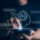 A hand points at a glowing digital illustration of a human head silhouette with an AI gear icon and chat bubbles floating around it on a dark background. Understanding what AI can and cannot do for your content is one of the most important things you can do to protect your SEO for therapists right now.