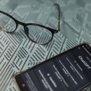 A smartphone displaying a ChatGPT conversation sits on a desk next to a pair of glasses. AI tools like ChatGPT can be helpful starting points for content creation, but therapists and helping professionals need more than AI output alone to build an effective SEO for therapists strategy.