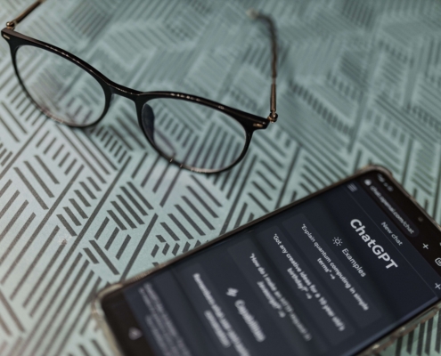 A smartphone displaying a ChatGPT conversation sits on a desk next to a pair of glasses. AI tools like ChatGPT can be helpful starting points for content creation, but therapists and helping professionals need more than AI output alone to build an effective SEO for therapists strategy.